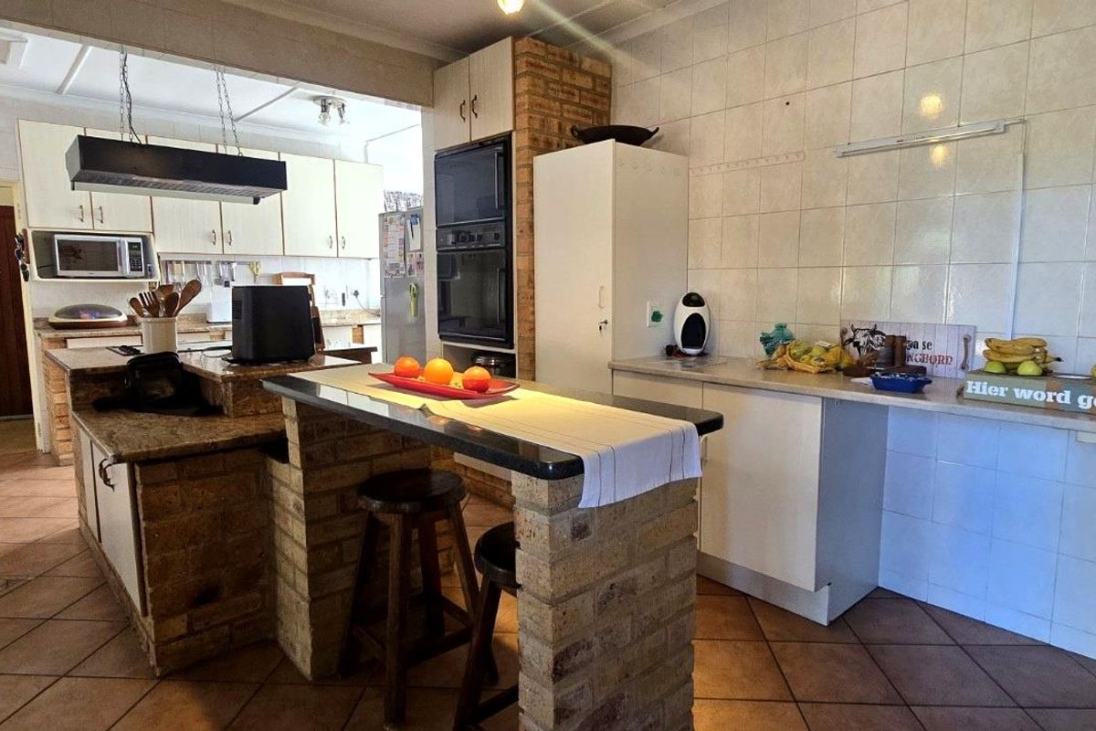 Spacious kitchen featuring brick breakfast bar, granite countertops, built-in oven, and tiled splashbacks, offering a functional layout with ample storage space.
