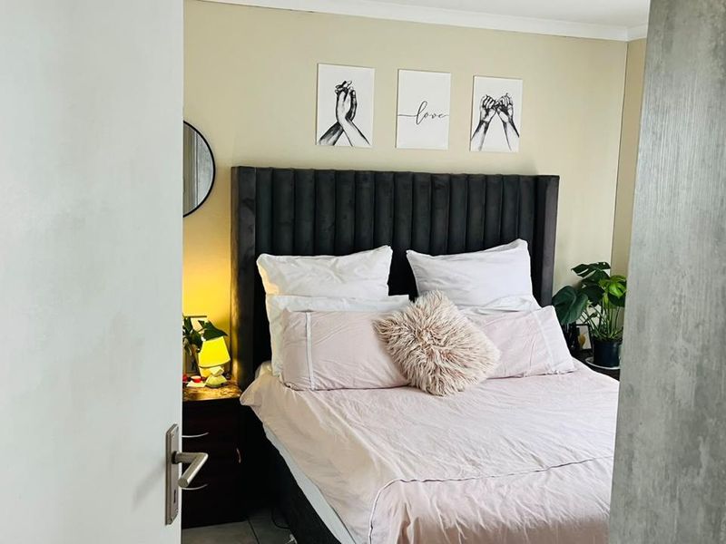A cozy bedroom featuring a neutral wall finish and a prominent upholstered headboard, viewed through a doorway.