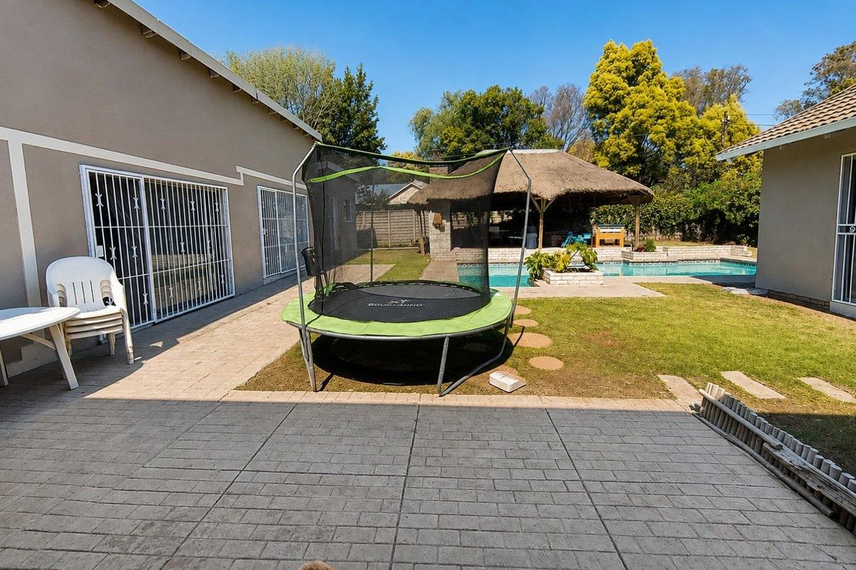 Rear garden area featuring a paved patio, swimming pool, and a thatched lapa, providing an outdoor entertainment space.