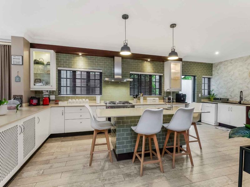 Modern kitchen featuring a central island, subway tile backsplash, stainless steel extractor fan, and ample built-in cabinetry with pendant lighting.