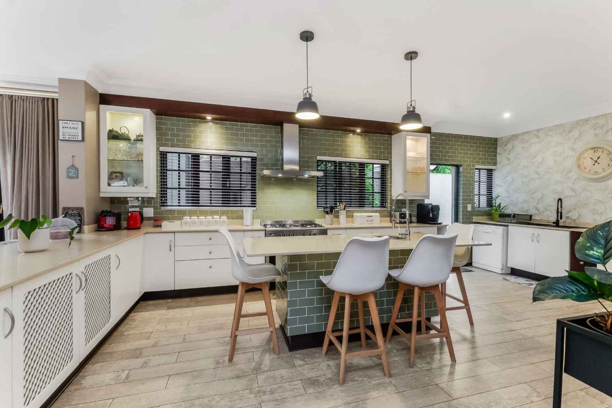 Modern kitchen featuring a central island, subway tile backsplash, stainless steel extractor fan, and ample built-in cabinetry with pendant lighting.