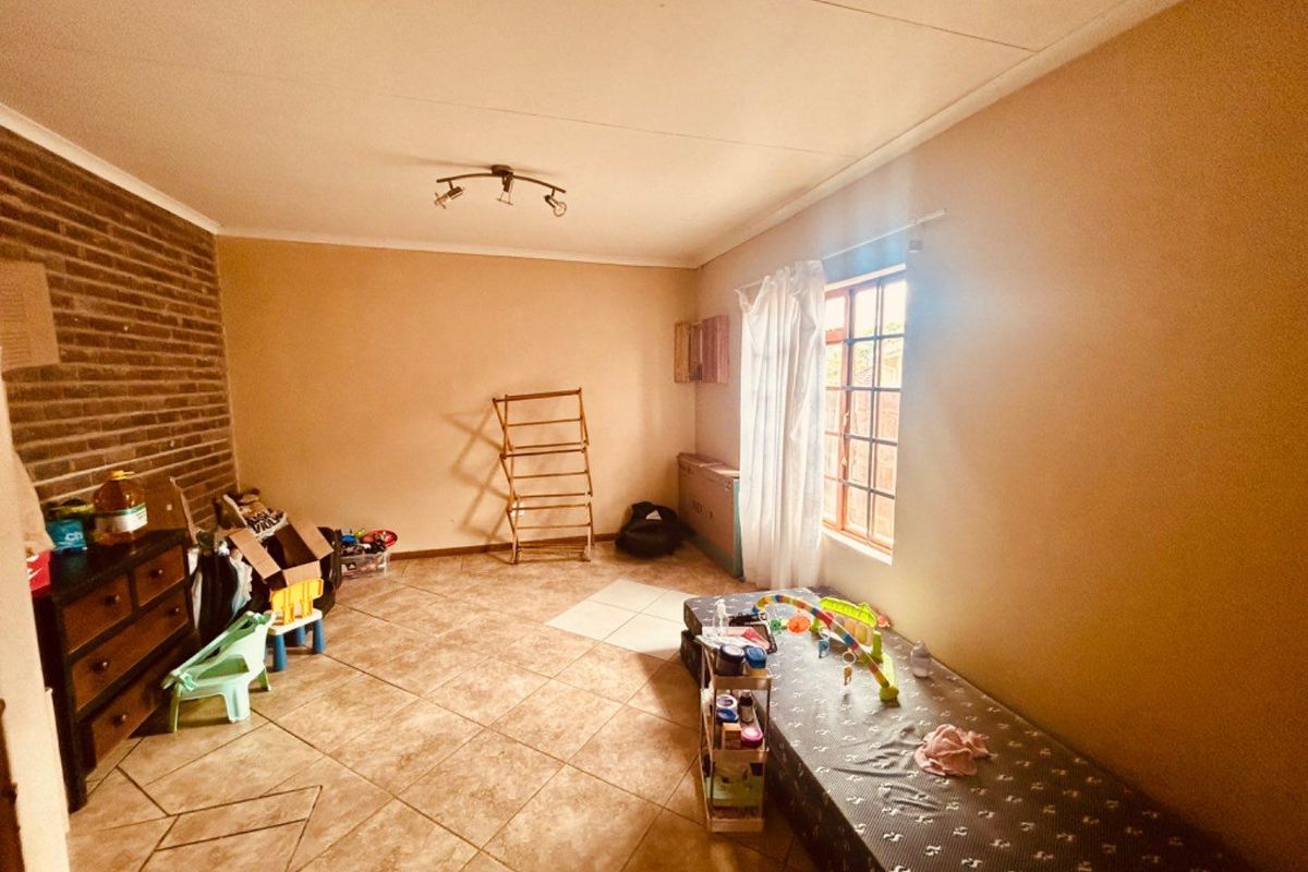 A bedroom featuring tiled flooring, a brick feature wall, and a window with natural light, offering a versatile space for customization.