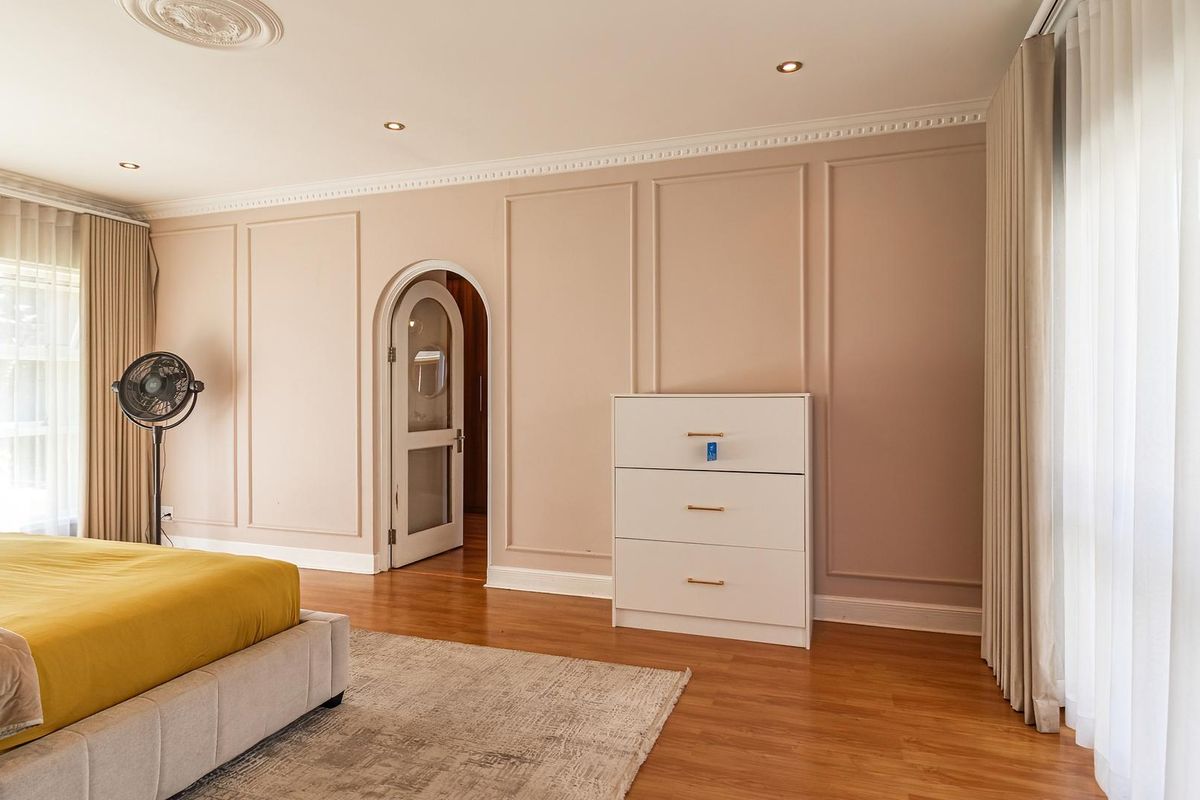 Spacious bedroom featuring elegant wainscoting, an arched doorway, hardwood flooring, and classic crown molding with a decorative ceiling rose.