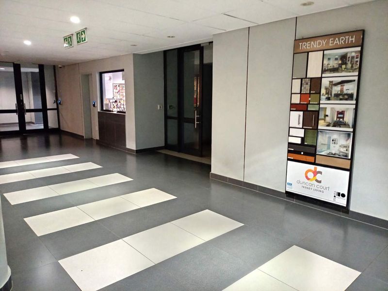 A clean, modern commercial-style hallway featuring tiled flooring, glass entrance doors, and a reception service window.