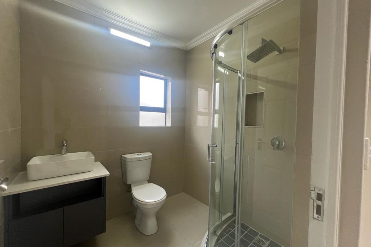 Modern bathroom featuring a glass-enclosed corner shower, wall-mounted vanity with vessel sink, and neutral floor-to-ceiling tiling.