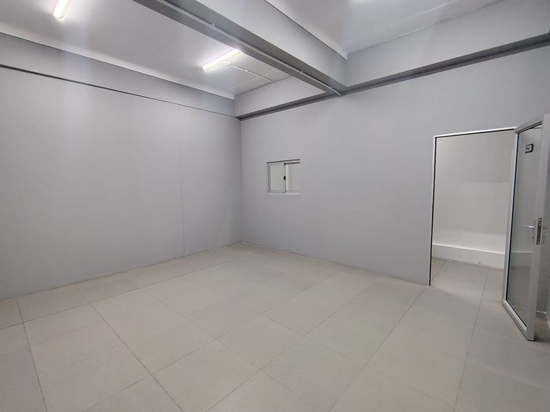 A clean, empty office space featuring neutral tiled flooring, bright overhead lighting, and a glass entrance door.