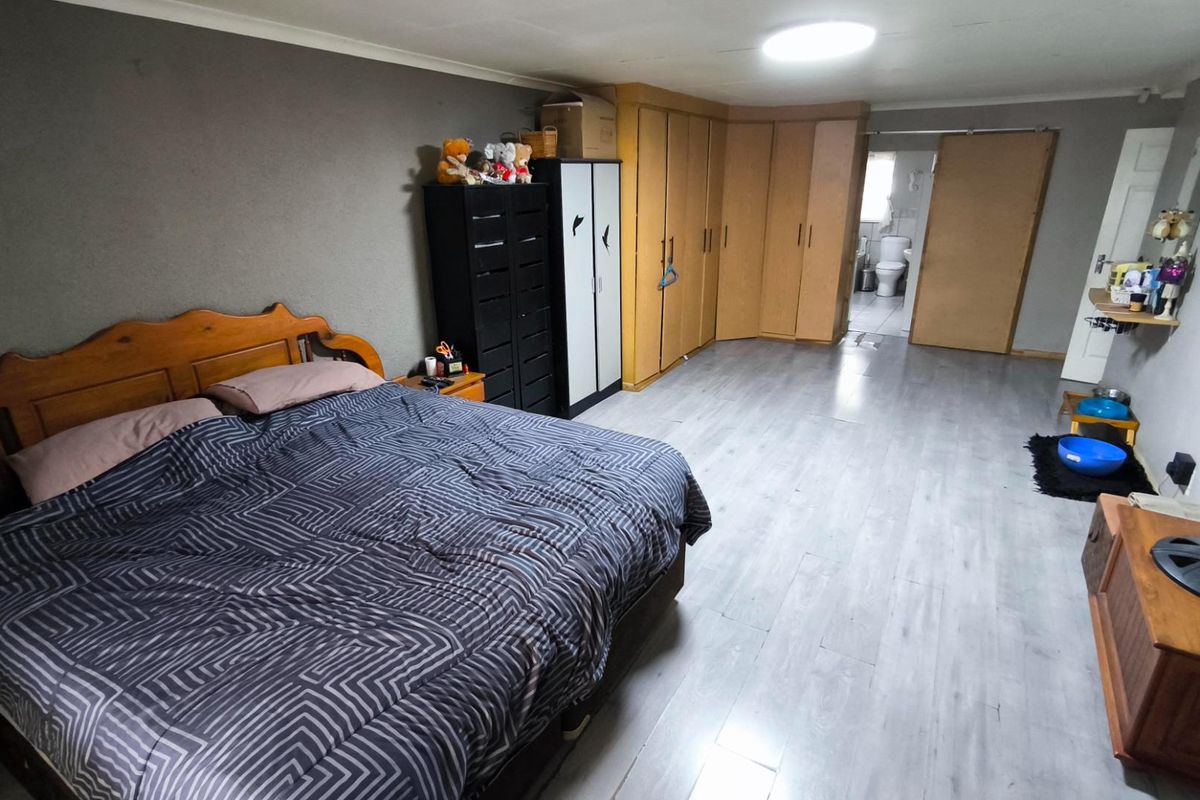 Spacious bedroom featuring built-in wooden cabinetry and an en-suite bathroom, finished with light-toned laminate flooring.