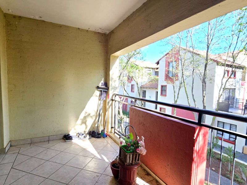 A covered balcony featuring tiled flooring and a metal balustrade, offering an outdoor space with views of the surrounding apartment complex.