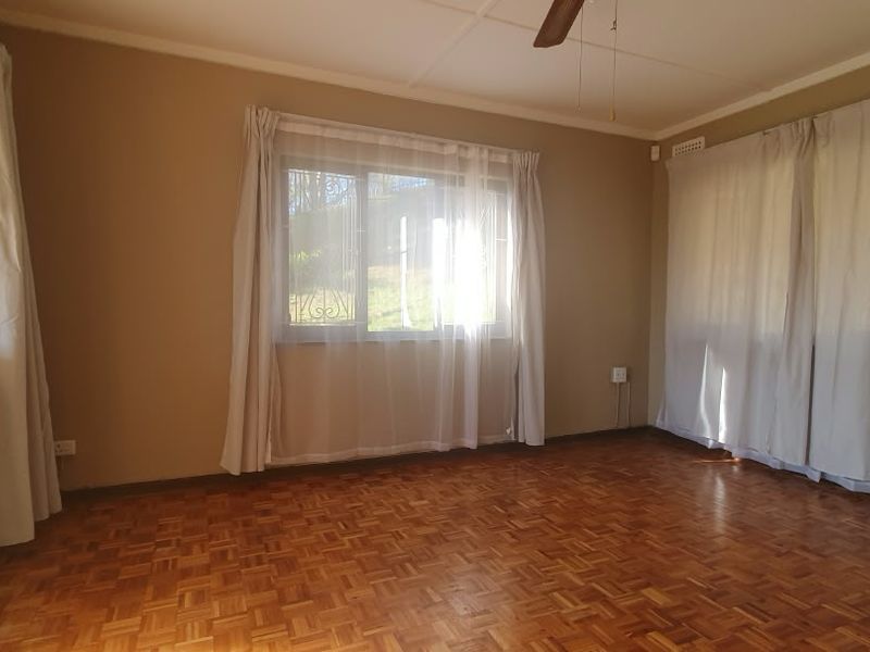 A spacious, empty living room featuring classic parquet flooring, a ceiling fan, and large windows with security bars, offering a bright and versatile living space.