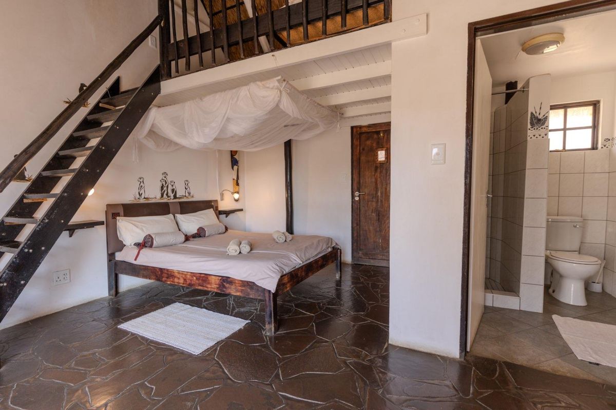 A rustic bedroom featuring a mezzanine level, stone flooring, and an en-suite bathroom with a shower and toilet.