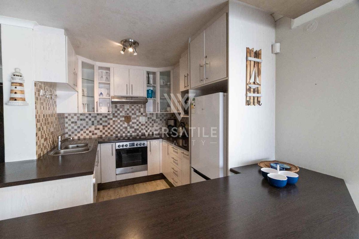 Compact kitchen featuring white cabinetry, dark laminate countertops, mosaic tile backsplash, built-in oven, extractor fan, and a breakfast bar counter.