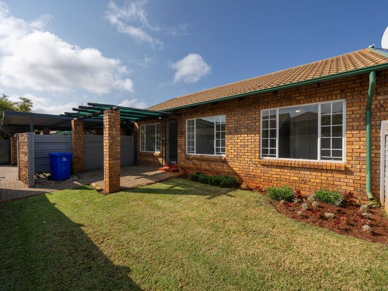 Rear view of the townhouse featuring a brick facade, tiled roof, paved patio area with a pergola, and a well-maintained garden lawn.