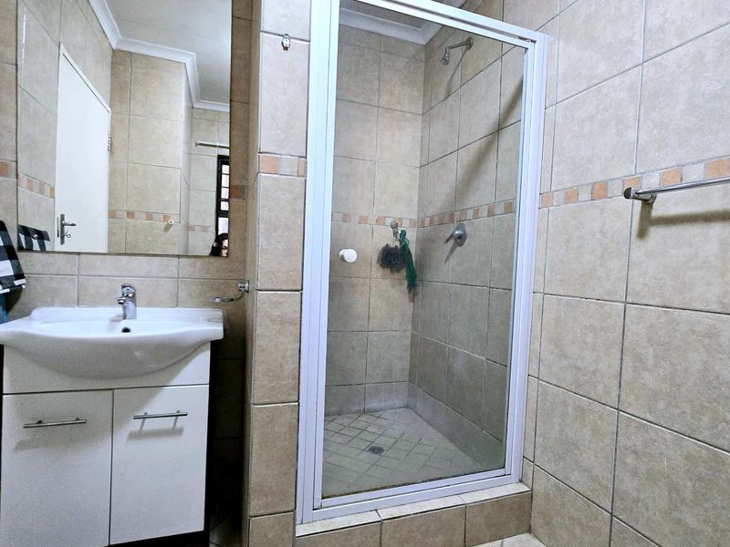 A functional bathroom featuring a vanity cabinet with basin, a glass-enclosed shower, and neutral wall tiling throughout.