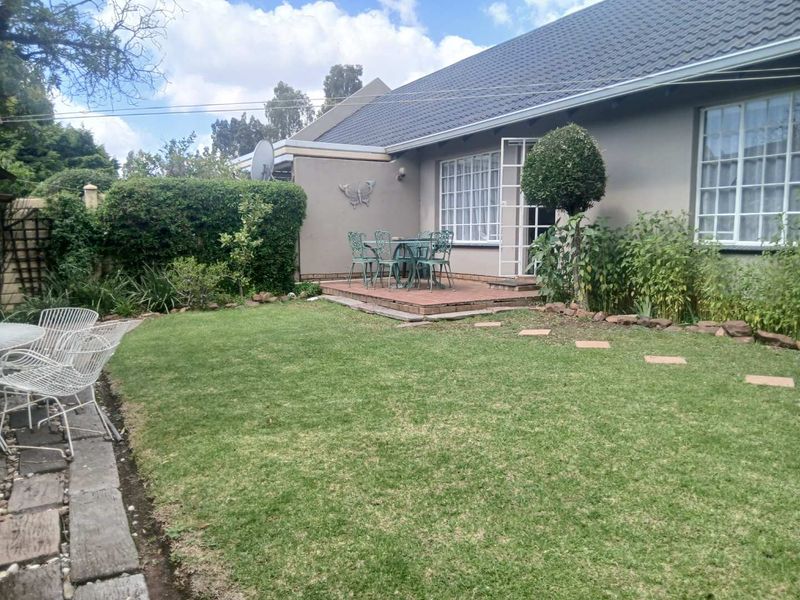 Rear view of the townhouse featuring a paved patio area, a well-maintained lawn, and established garden borders.