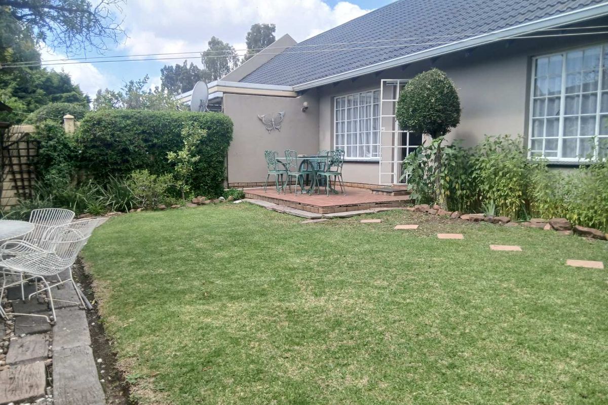 Rear view of the townhouse featuring a paved patio area, a well-maintained lawn, and established garden borders.