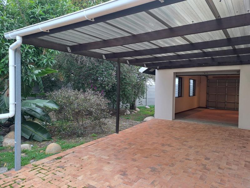 A covered patio area featuring brick paving and a timber pergola structure, providing direct access to the adjacent garage.