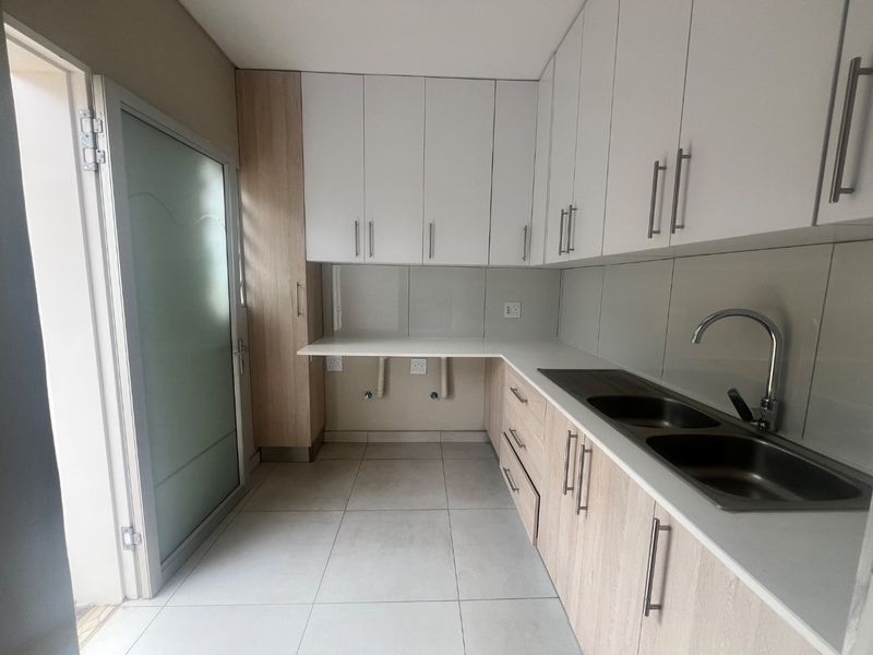 A clean and modern laundry room featuring ample built-in cabinetry, a double stainless steel sink, and dedicated plumbing connections for appliances.