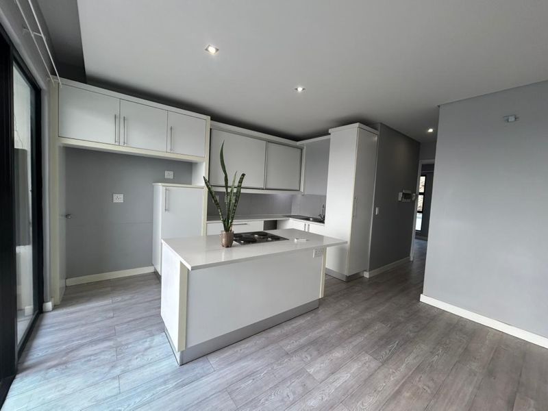 Modern open-plan kitchen featuring white cabinetry, a central island with a built-in hob, and light grey laminate flooring.