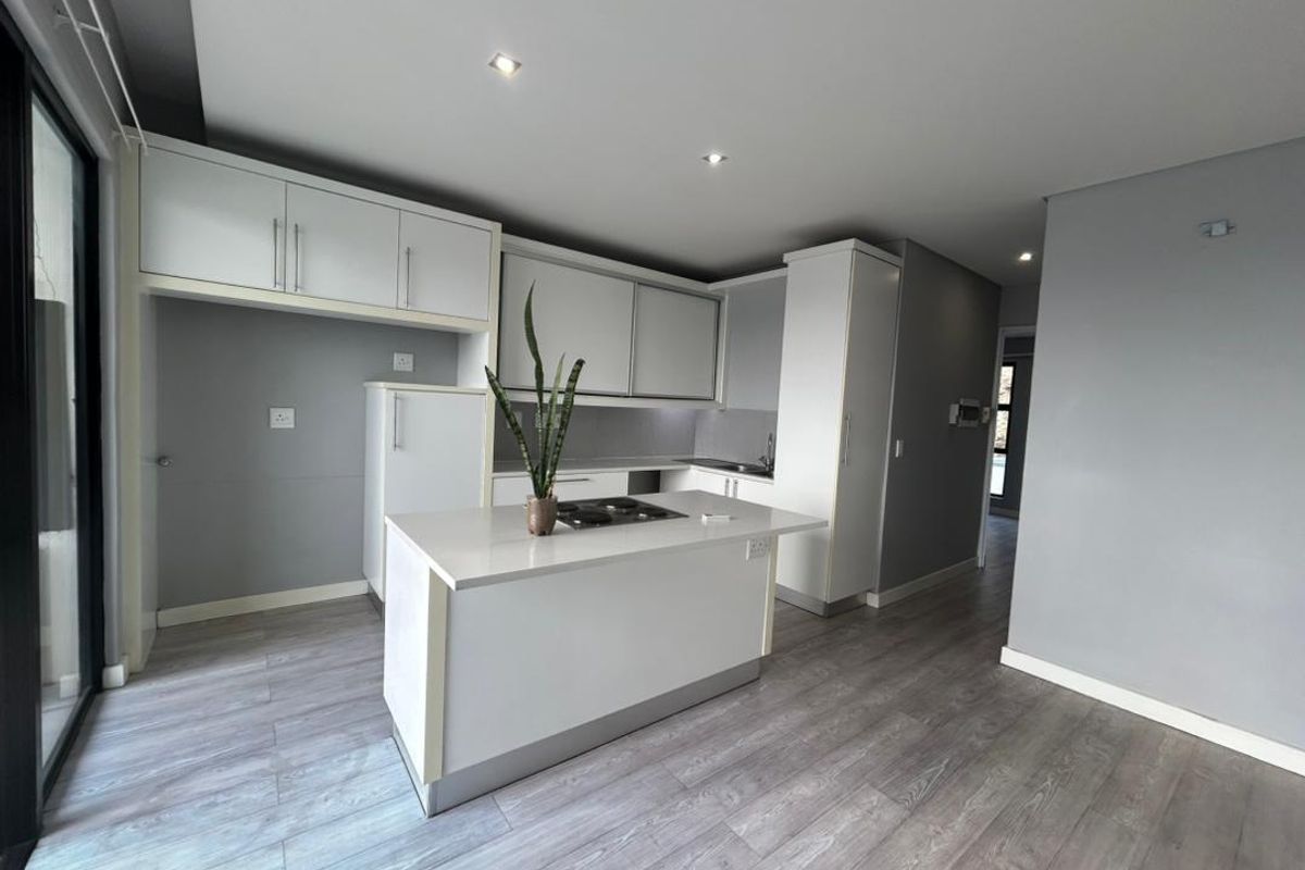 Modern open-plan kitchen featuring white cabinetry, a central island with a built-in hob, and light grey laminate flooring.