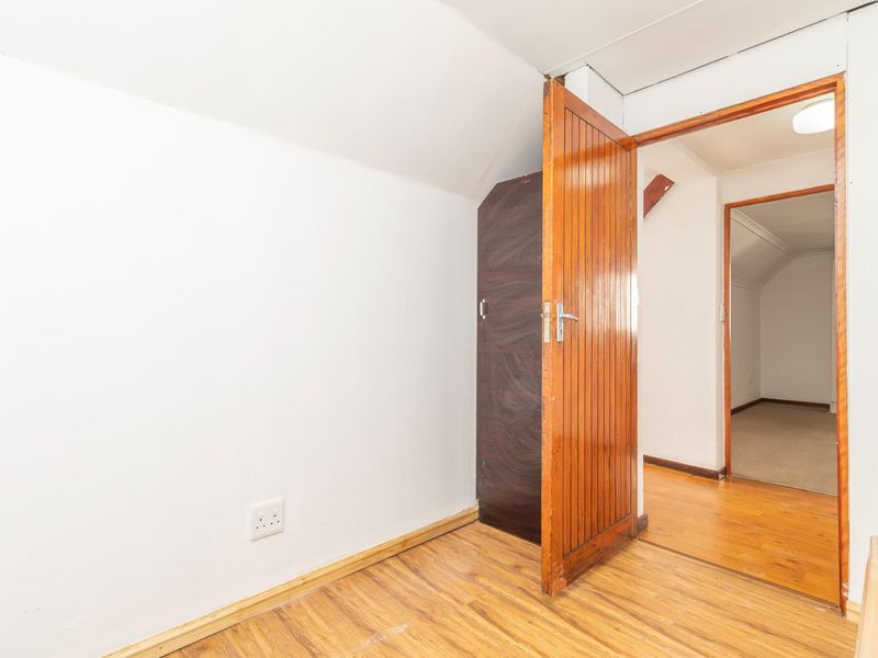 An empty bedroom featuring laminate flooring, a timber door, and a sloped ceiling, offering a blank canvas for renovation or interior design.