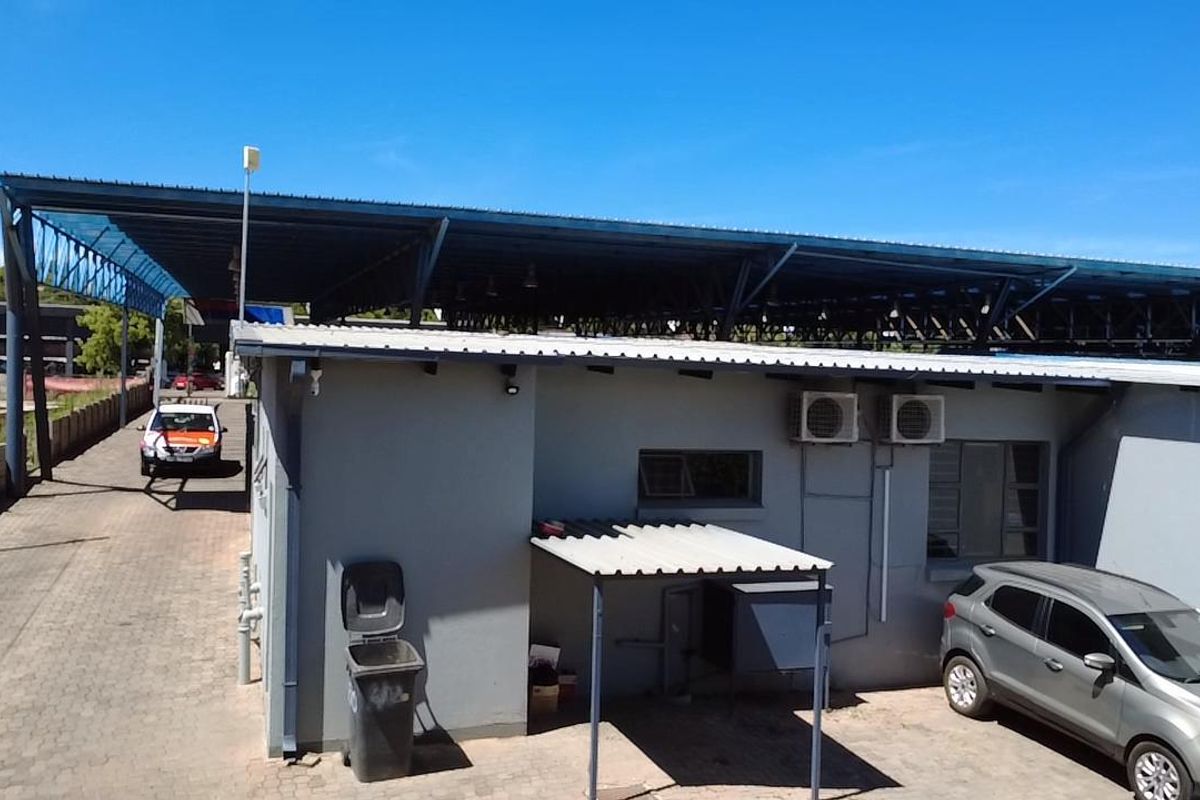 Rear exterior view of a commercial property featuring a large metal roof structure, paved driveway, and wall-mounted air conditioning units.