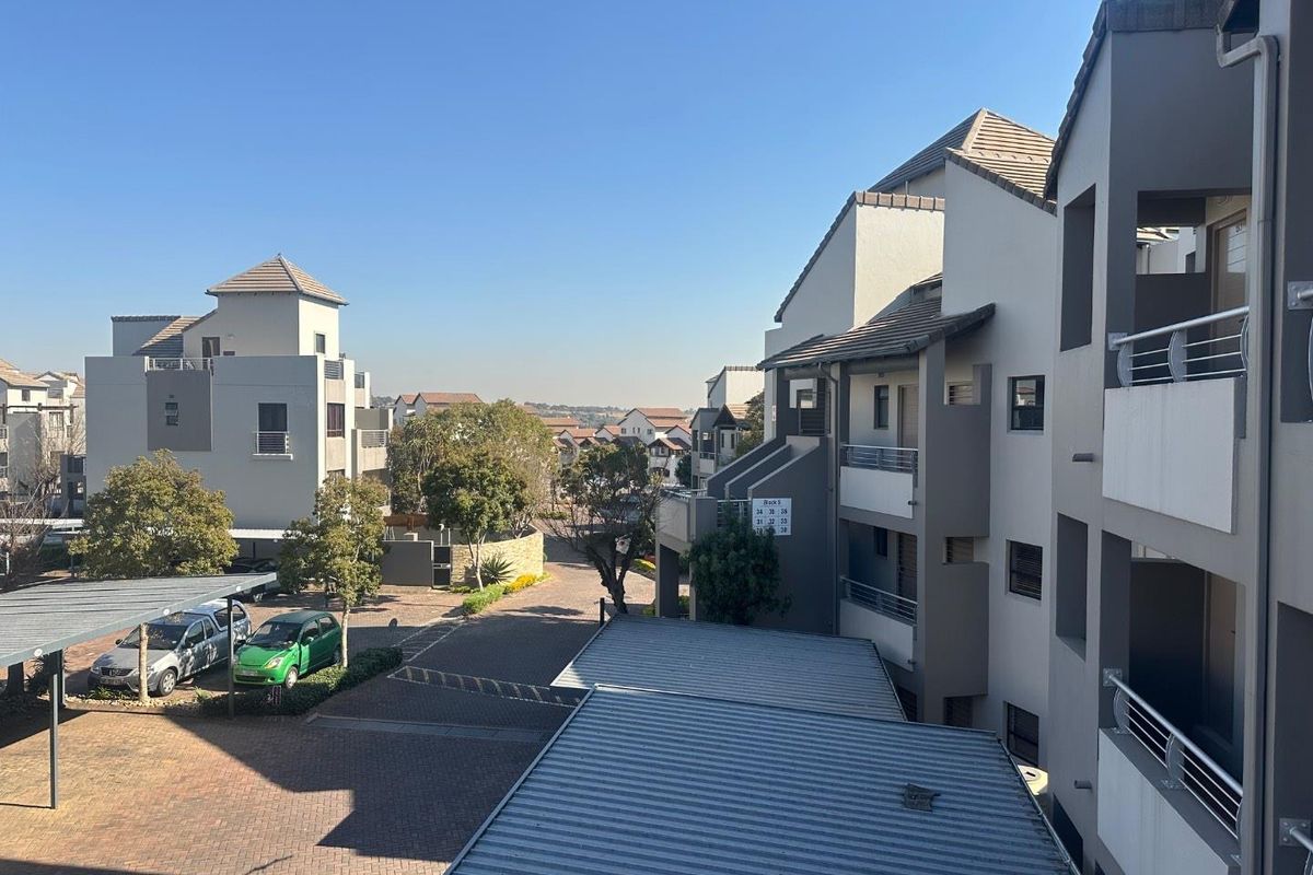 An elevated view of the apartment complex grounds, featuring paved driveways, covered carports, and multi-story residential blocks with balconies.