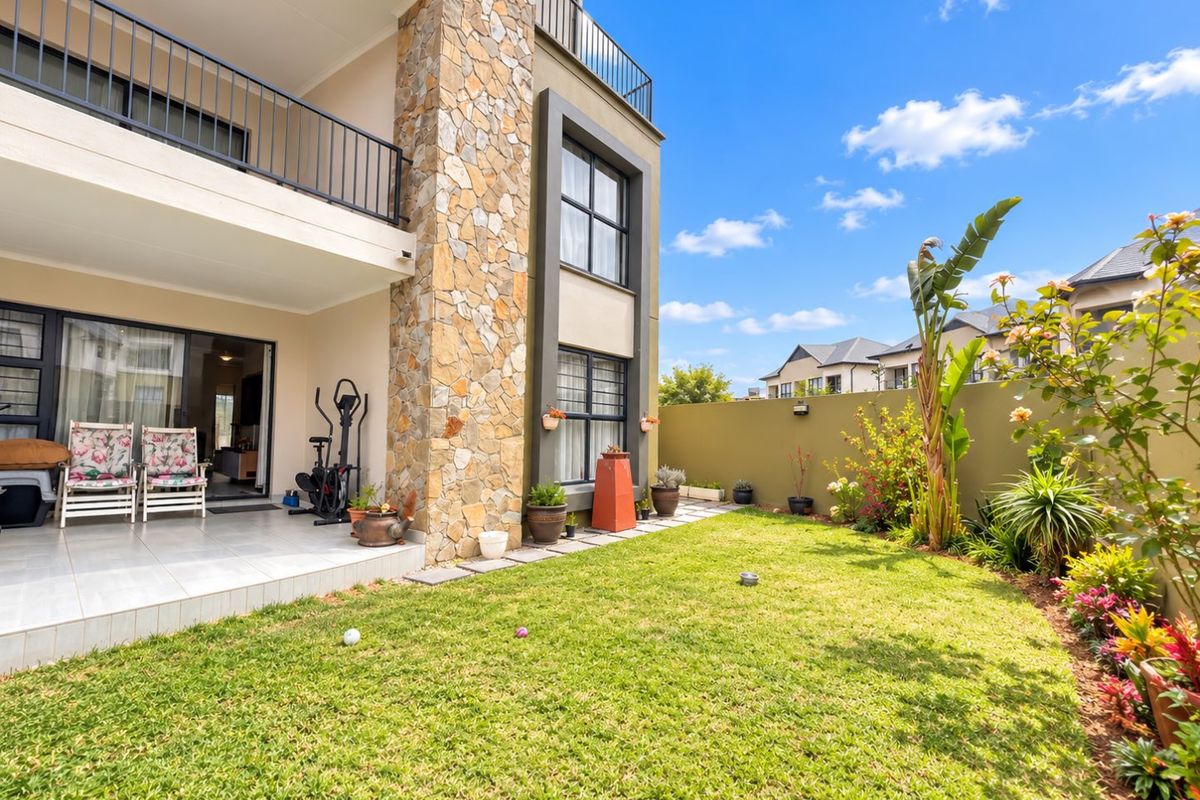 A well-maintained rear exterior featuring a tiled patio, stone-clad pillar, balcony, and a private landscaped garden with a boundary wall.