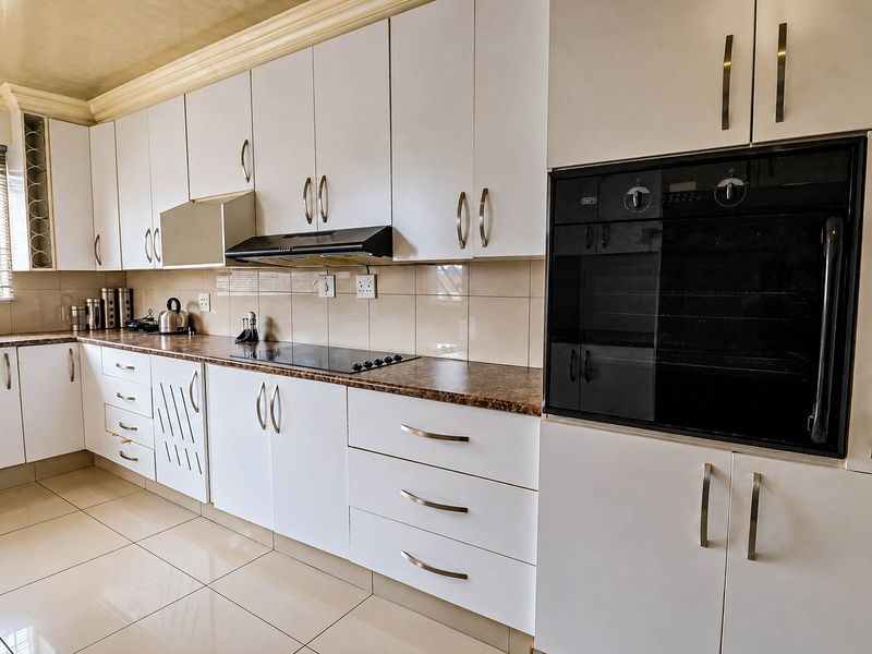 Modern kitchen featuring white cabinetry, built-in oven, extractor fan, ceramic hob, laminate countertops, and tiled flooring.