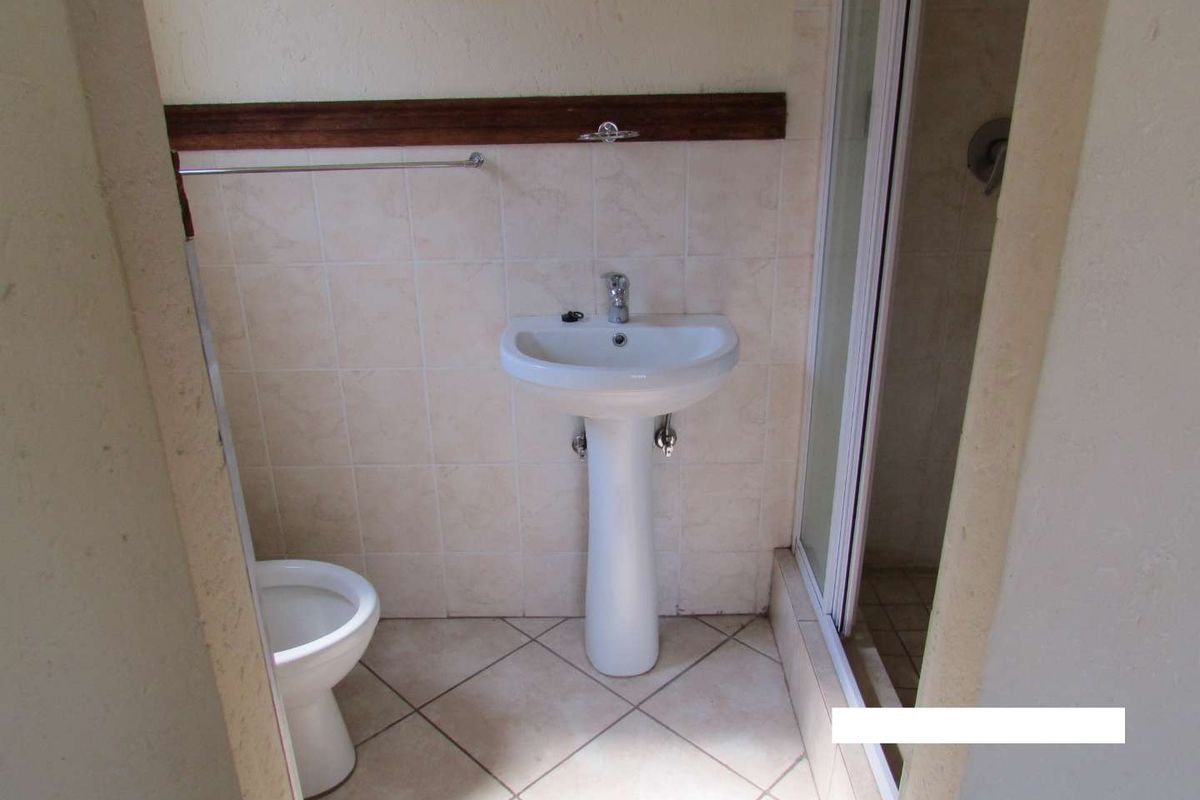 A functional bathroom featuring a pedestal basin, toilet, and a shower enclosure with neutral ceramic tiling throughout.
