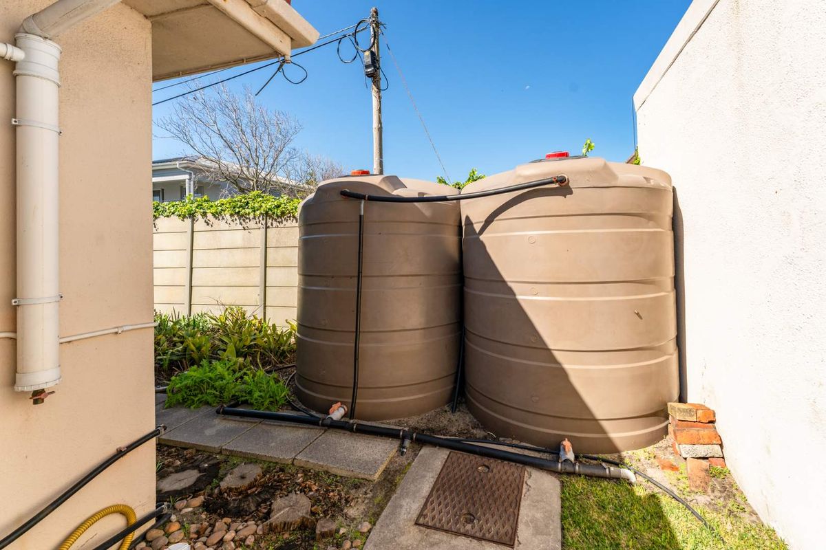 Exterior side area featuring two large plastic water storage tanks connected with plumbing infrastructure, situated against a boundary wall.