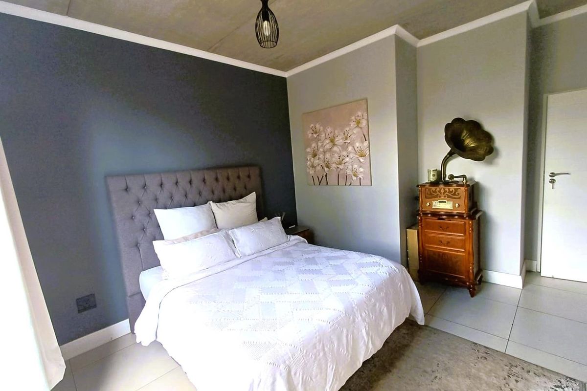 A modern bedroom featuring a raw concrete ceiling, tiled flooring, and a feature wall, creating a contemporary and stylish living space.