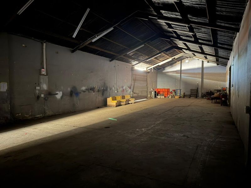 Spacious industrial utility area featuring exposed timber roof trusses, concrete flooring, and a large roller shutter door, suitable for storage or workshop use.