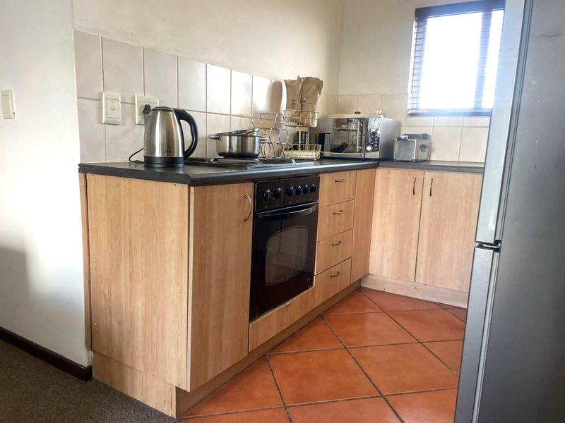Compact kitchen featuring light wood-look cabinetry, dark laminate countertops, built-in oven, hob, and terracotta floor tiles with a tiled splashback.
