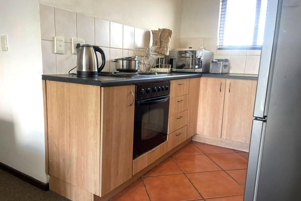 Compact kitchen featuring light wood-look cabinetry, dark laminate countertops, built-in oven, hob, and terracotta floor tiles with a tiled splashback.
