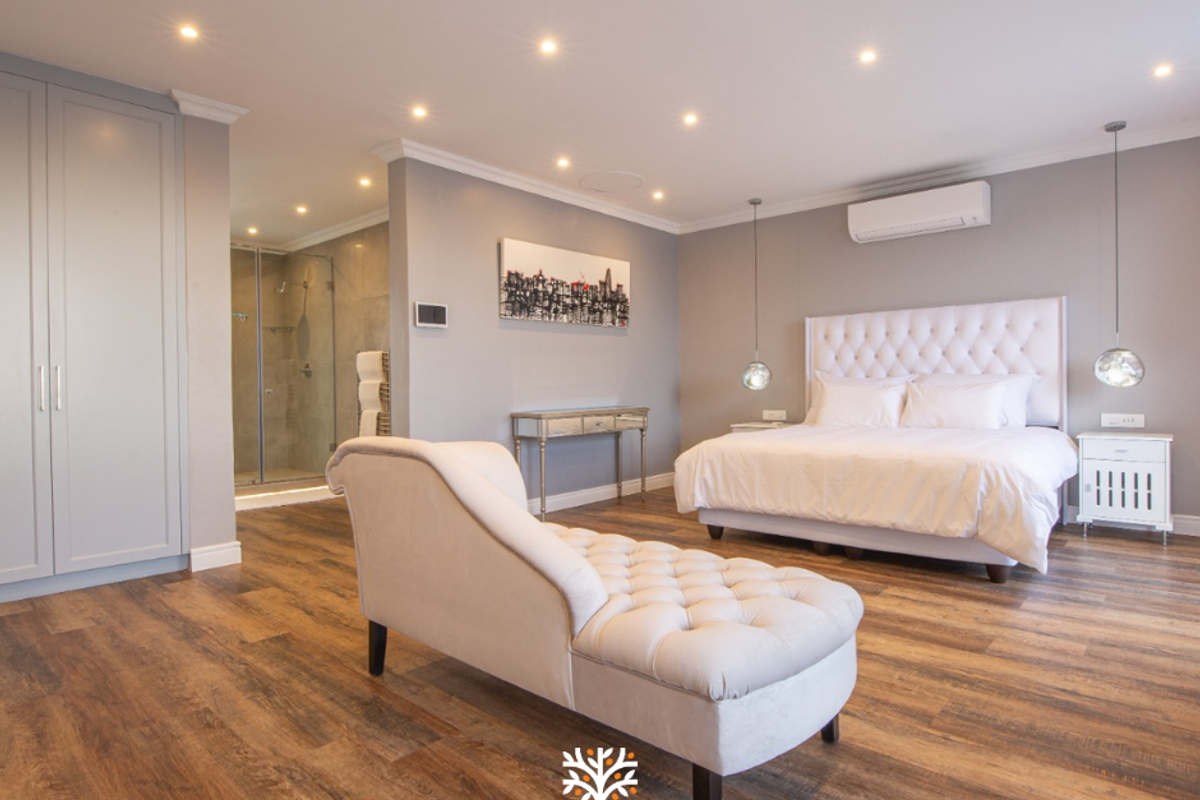 Spacious bedroom featuring wood-look flooring, recessed ceiling lighting, integrated wardrobe, and an en-suite bathroom with a glass-enclosed shower.