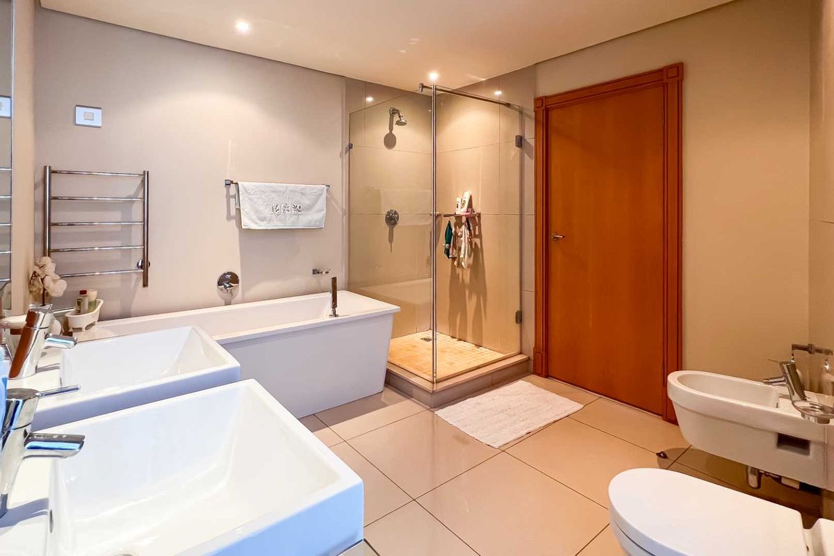 Modern bathroom featuring a double vanity, freestanding bathtub, glass-enclosed shower, bidet, and wall-mounted toilet with neutral tile finishes.
