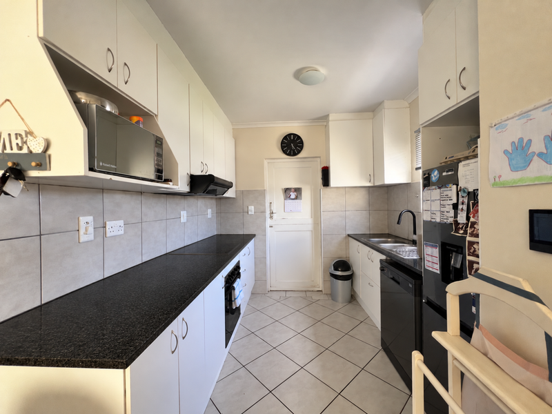 A functional galley-style kitchen featuring white cabinetry, dark countertops, tiled backsplash, and integrated appliances, offering a clean and practical workspace.