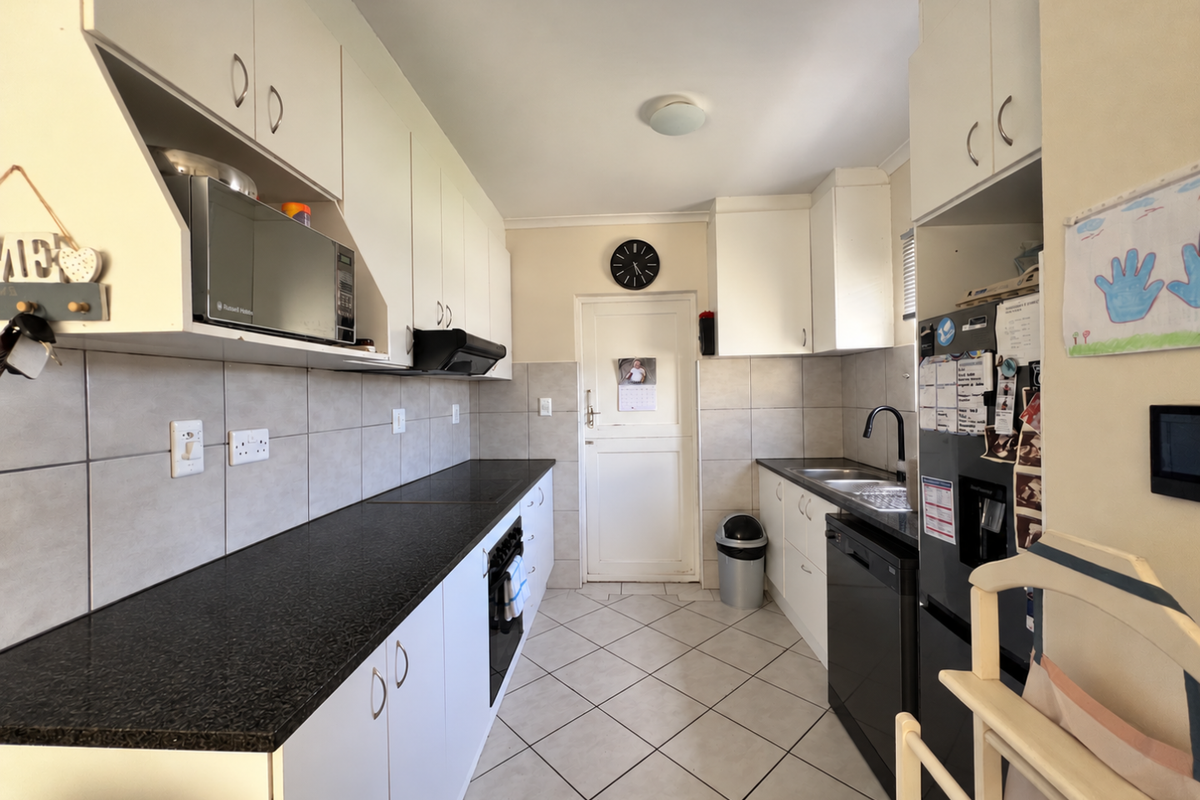 A functional galley-style kitchen featuring white cabinetry, dark countertops, tiled backsplash, and integrated appliances, offering a clean and practical workspace.