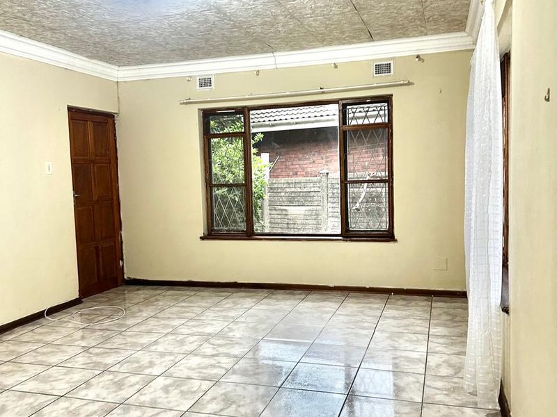 An empty living room featuring tiled flooring, a decorative pressed metal ceiling, and timber window frames, offering a blank canvas for personalization.
