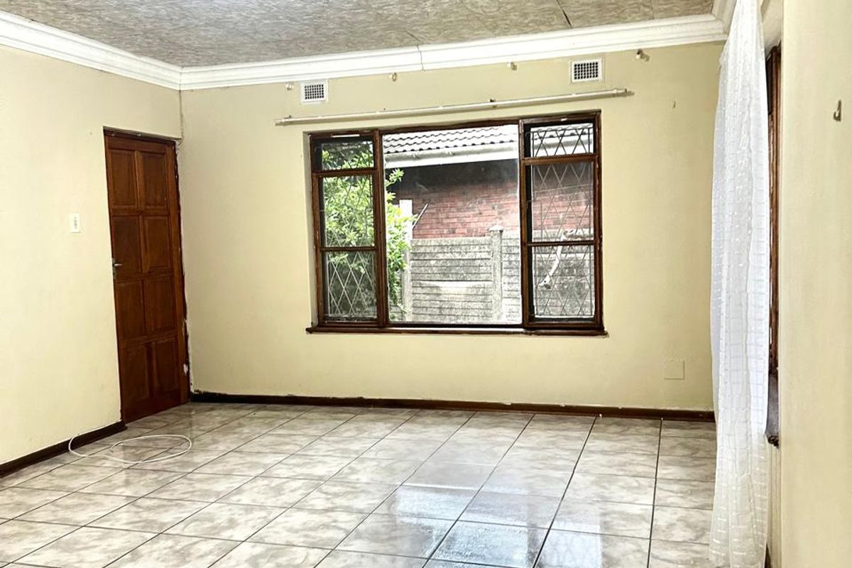 An empty living room featuring tiled flooring, a decorative pressed metal ceiling, and timber window frames, offering a blank canvas for personalization.