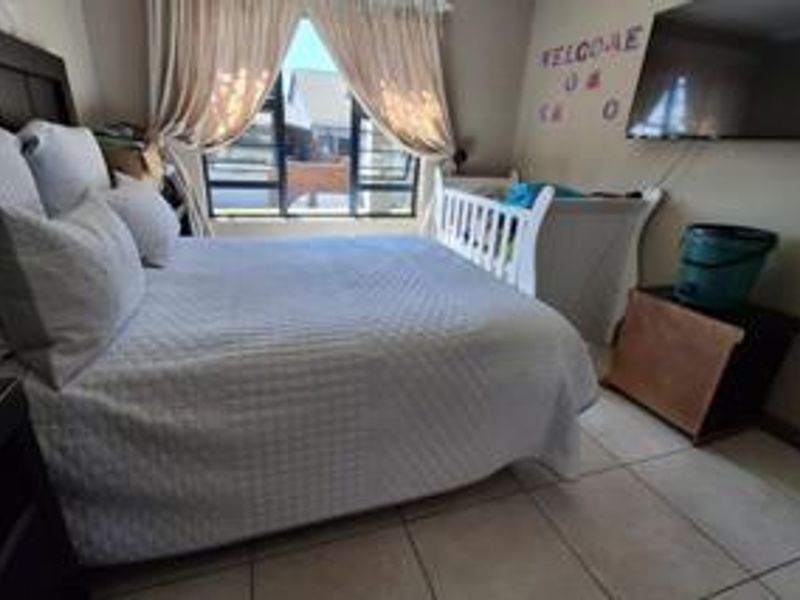 A bedroom featuring tiled flooring and large windows with curtains, providing natural light and a view of the exterior.
