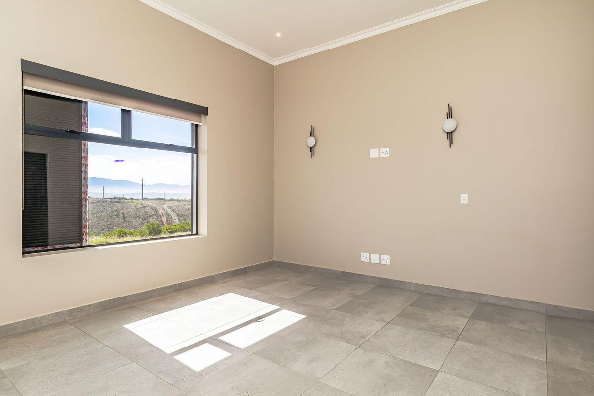 A bright, empty living room featuring large windows with scenic views, neutral wall tones, modern wall-mounted light fixtures, and tiled flooring.