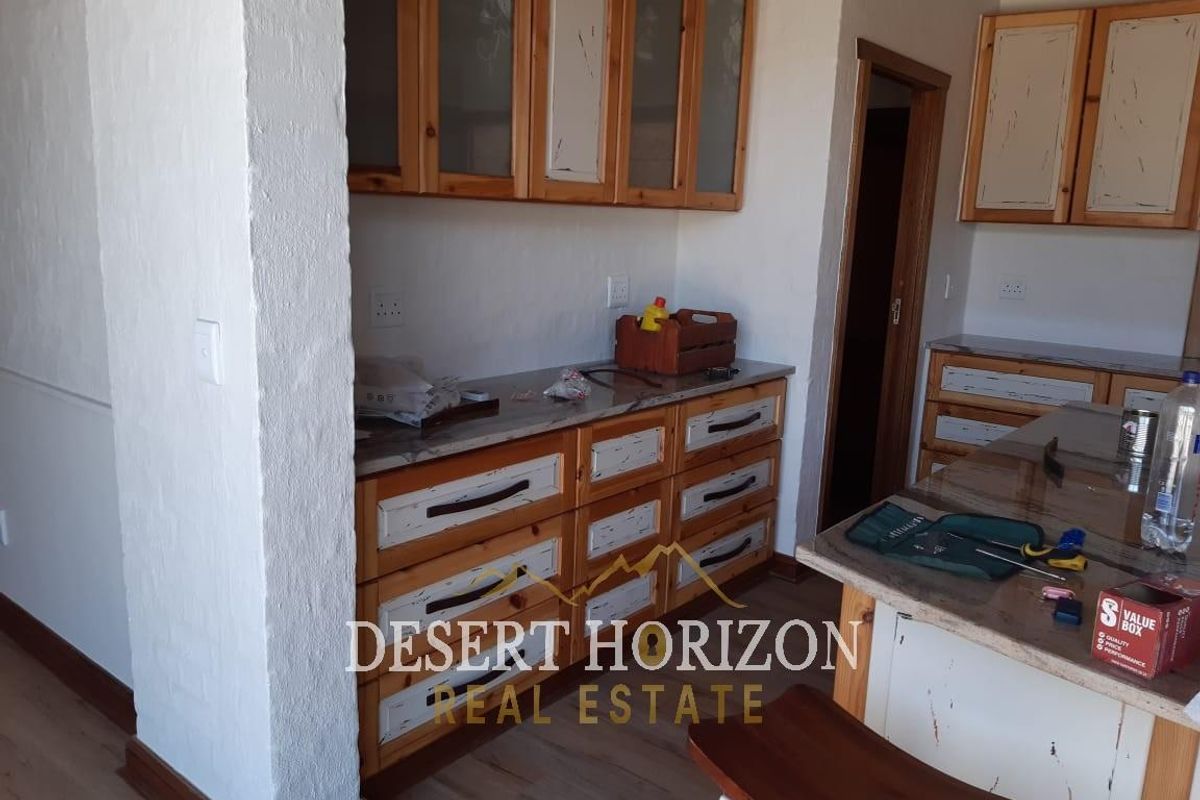 A functional kitchen area featuring wooden cabinetry, stone-look countertops, and a breakfast bar, showing signs of wear and dated finishes.