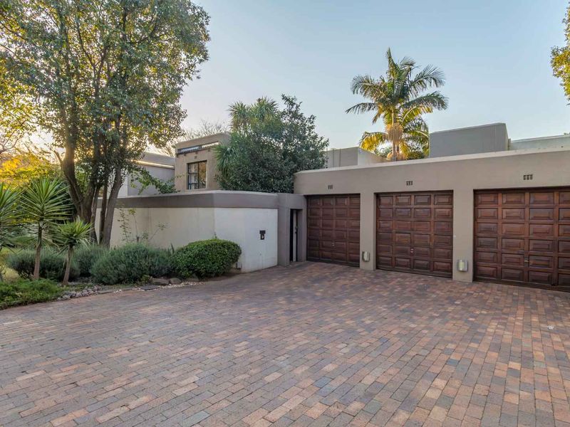 Front view of the property featuring a triple garage with wooden doors and a spacious paved driveway, surrounded by established garden landscaping.