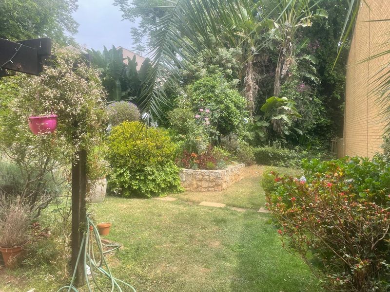 A lush, private garden area featuring a stone-clad raised planter bed, established greenery, and a well-maintained lawn adjacent to the building exterior.