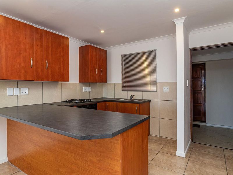 A functional kitchen featuring wooden cabinetry, dark laminate countertops, a gas hob, and tiled finishes, offering a clean and practical workspace.