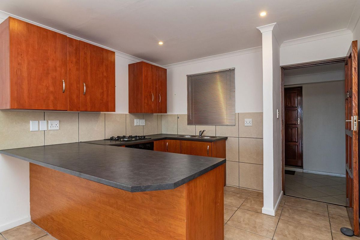 A functional kitchen featuring wooden cabinetry, dark laminate countertops, a gas hob, and tiled finishes, offering a clean and practical workspace.