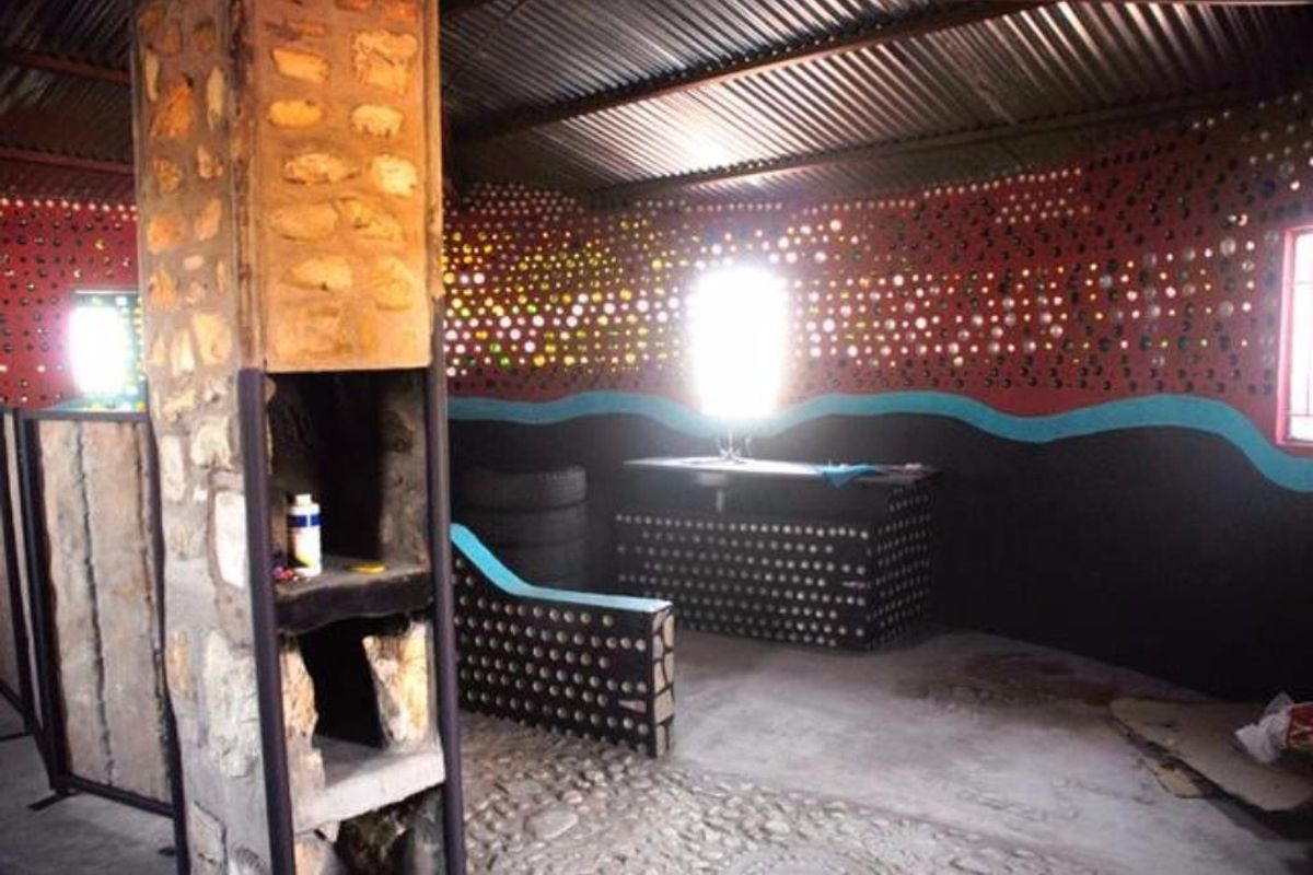 Unique interior space featuring unconventional bottle-wall construction, stone pillar, and corrugated metal roofing, offering a rustic and artistic aesthetic.