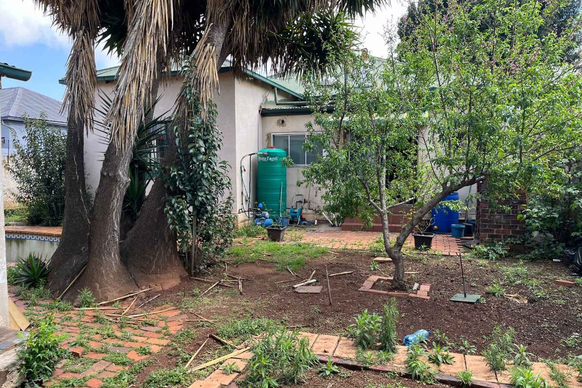 Rear exterior view of the property featuring a garden area, mature trees, brick paving, and a water storage tank.