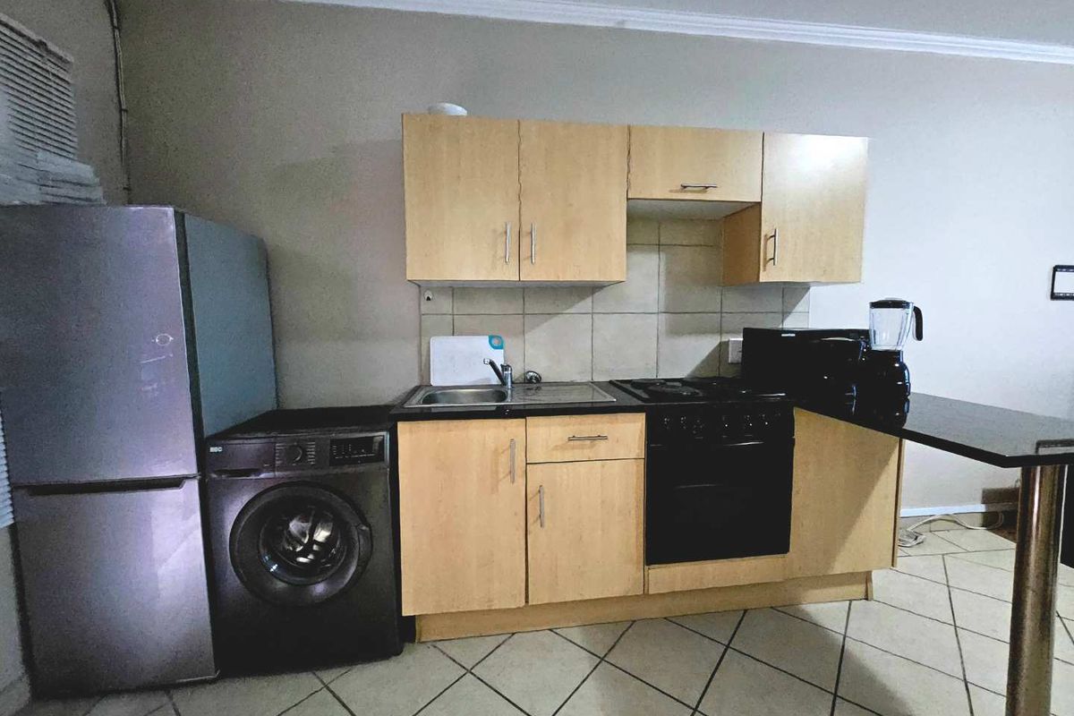 Compact kitchen featuring light wood cabinetry, a built-in oven and hob, tiled backsplash, and integrated space for laundry appliances.